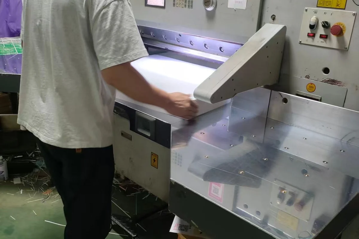 An operator handling a stack of paper at a cutting workstation.