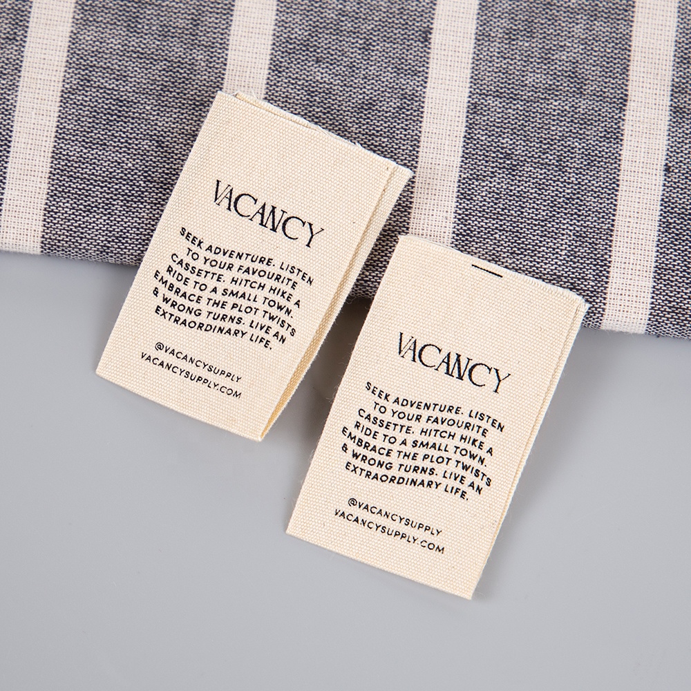 Two cream fabric labels with a brand name and several lines of black printed wording.