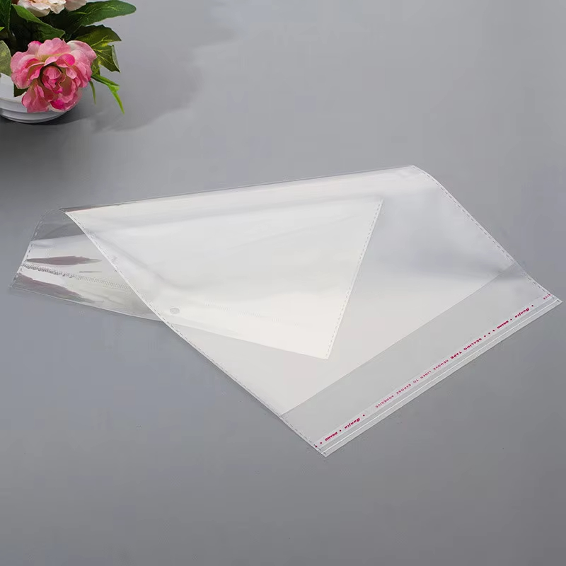 Clear garment bags with adhesive-flap closures laid flat on a gray surface.