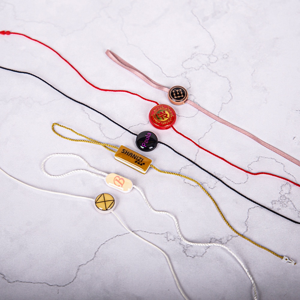 Several colored hang tag cords with round and rectangular locking pieces on a pale surface.