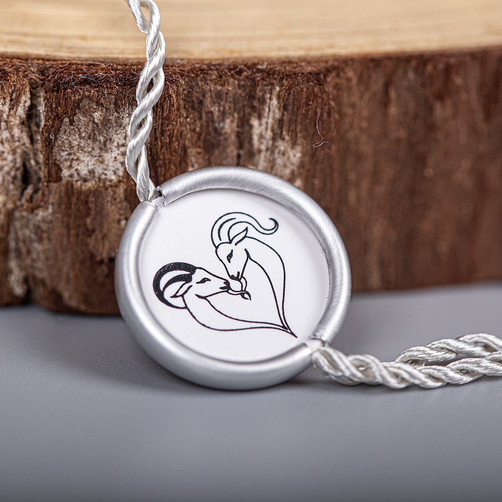 A silver-colored twisted tag cord connected to a round logo seal beside a wood block.