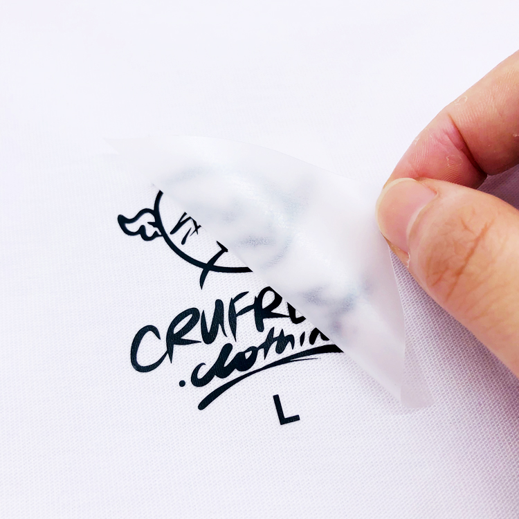 A hand lifting a translucent carrier from a black logo and size marking on white fabric.