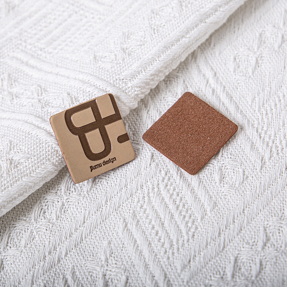 Two small brown leather-look label samples showing a decorated face and a plain reverse.