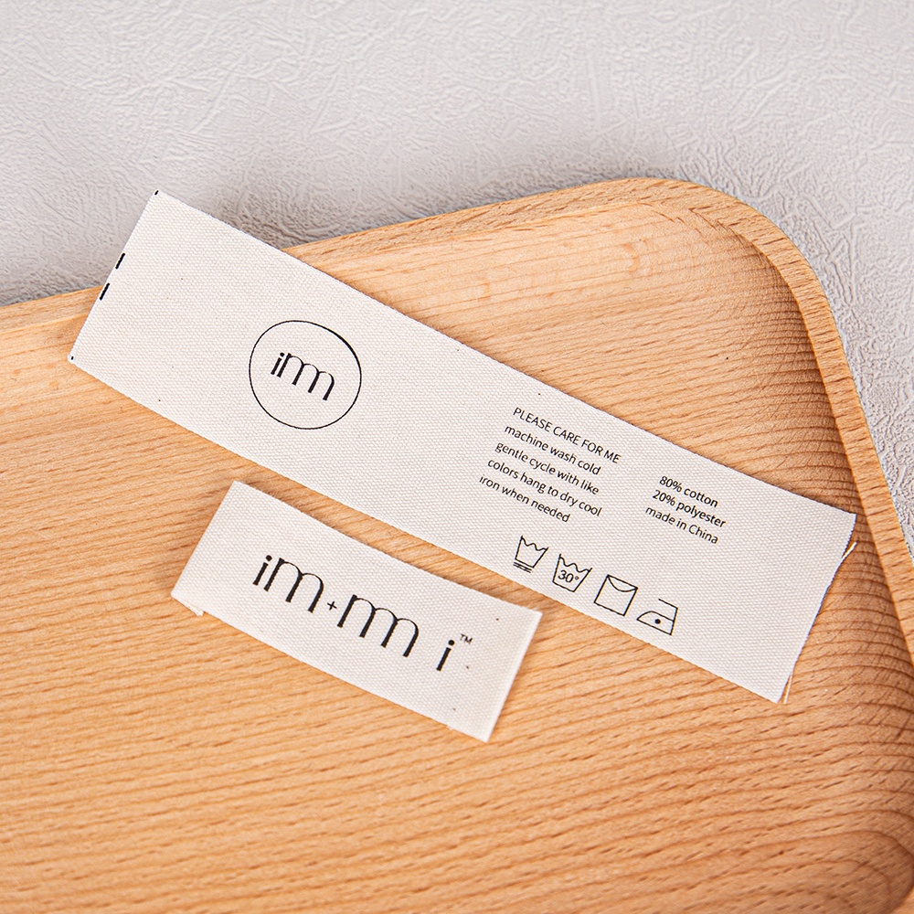 Two cream printed fabric labels, including a long label with care information.