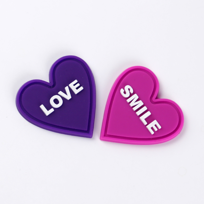 Purple and pink heart-shaped PVC label samples with raised white words and molded rims.