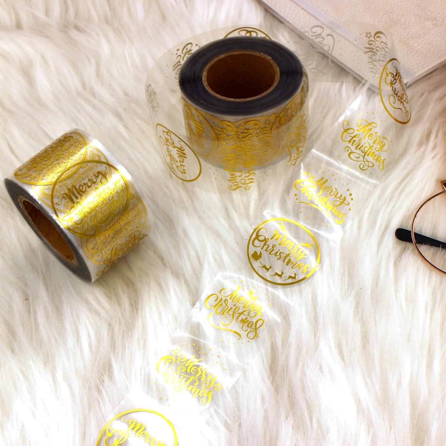 Rolls of clear round stickers carrying gold-colored Merry Christmas messages.
