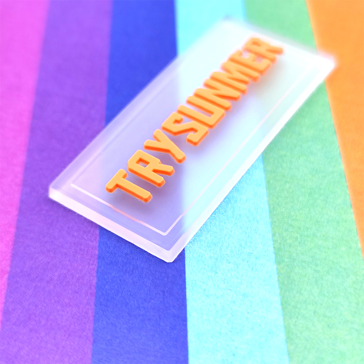 An orange raised wordmark on a transparent rectangular label over colored fabric.