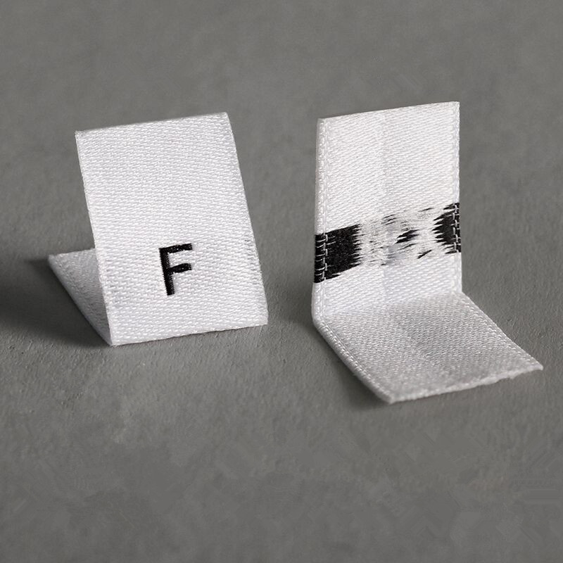 Front and reverse of white folded fabric size labels with black markings.
