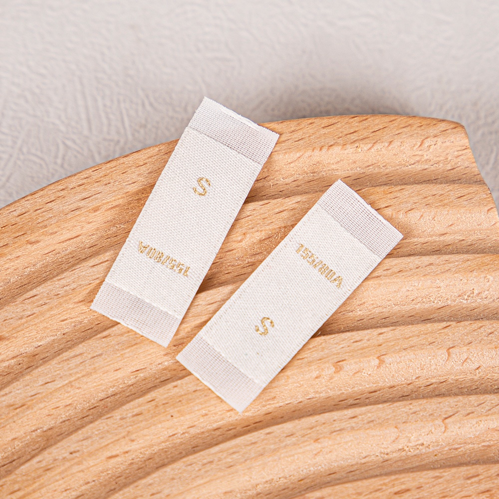 Two white fabric size labels with gold markings and blank sewing ends.