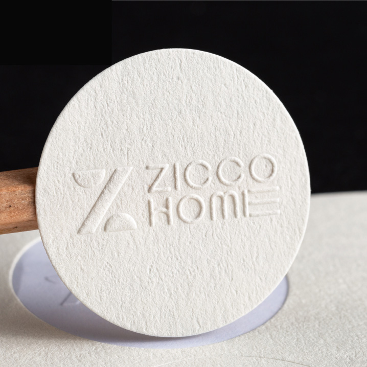 Round white textured paper sticker with an embossed brand name.