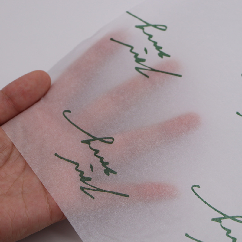 A hand behind translucent tissue paper printed with repeating green lettering.