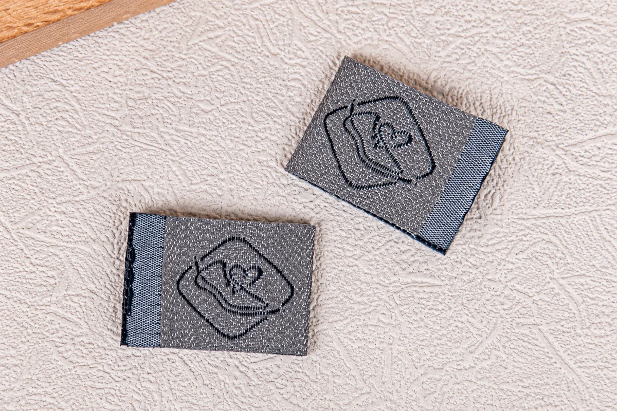 Gray woven brand-label samples on a continuous textured fabric background.