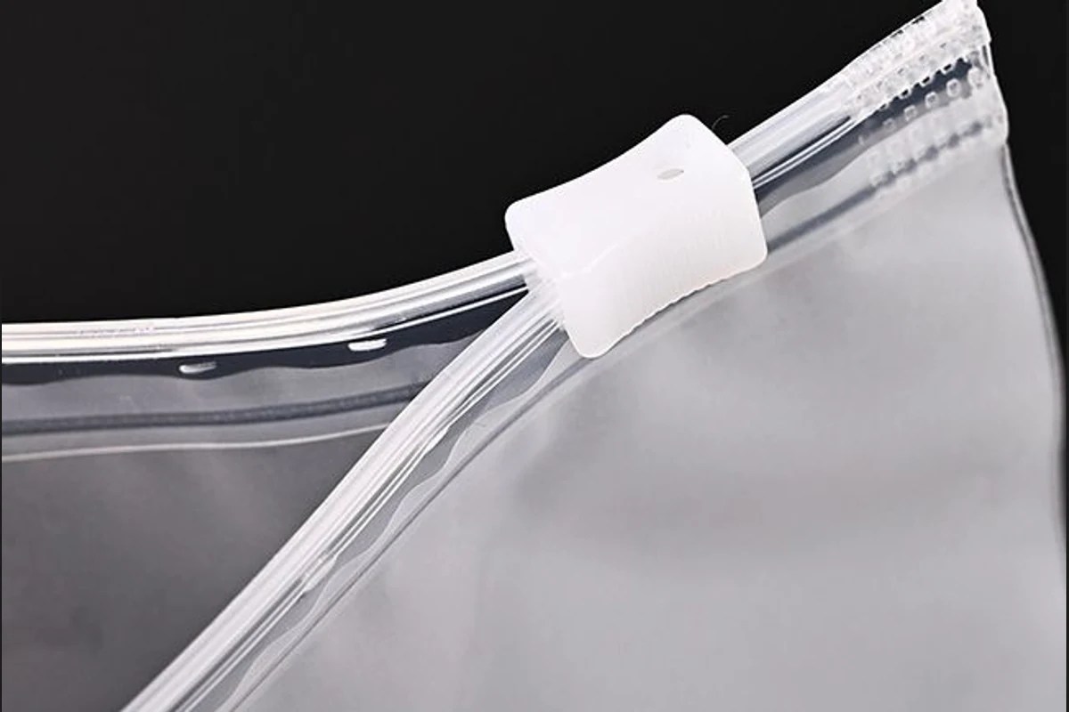 Close-up of a white slider and the zipper tracks on a transparent garment bag.