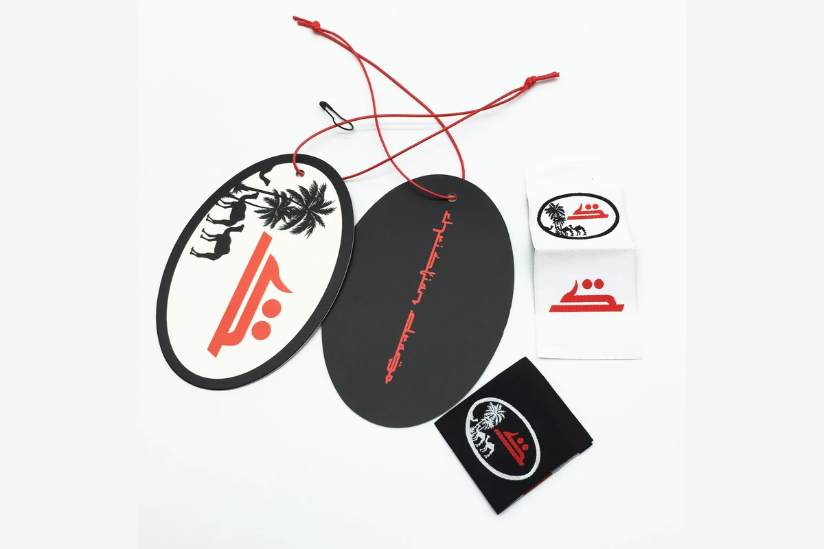 Two oval paper hang tags with red cords, shown beside matching black and white fabric labels.