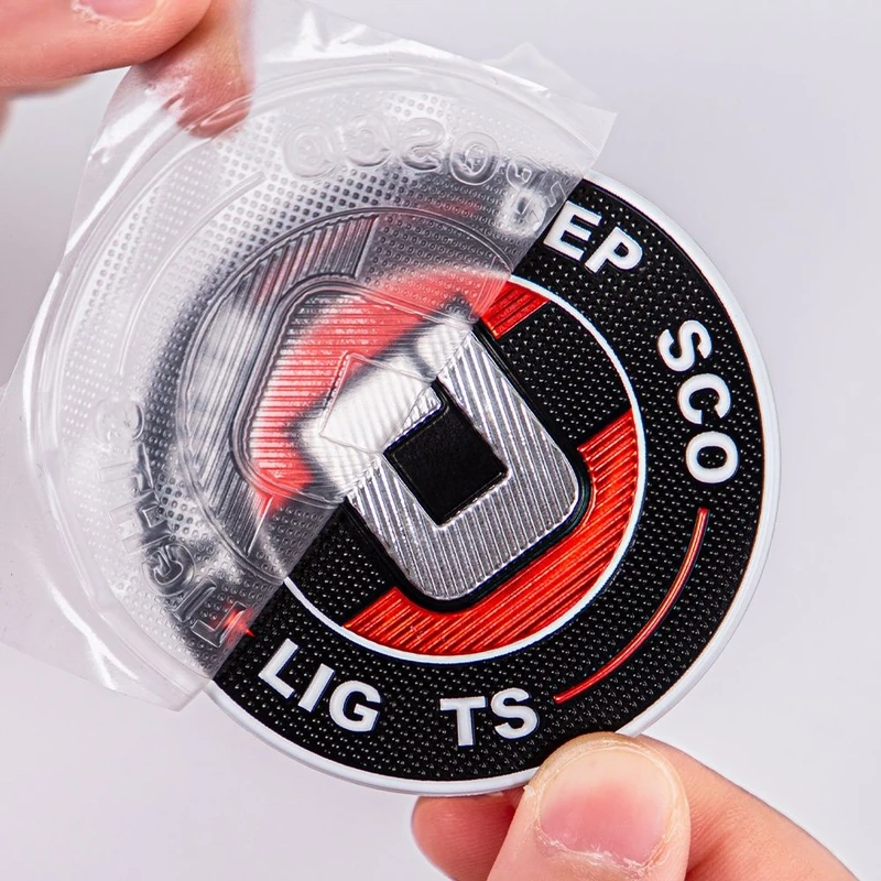 A glossy round transfer label with black, red and silver details and a peeled carrier film.