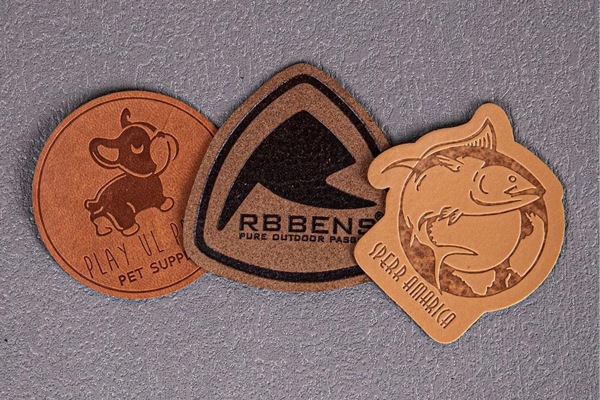 Three shaped leather label samples with impressed artwork.