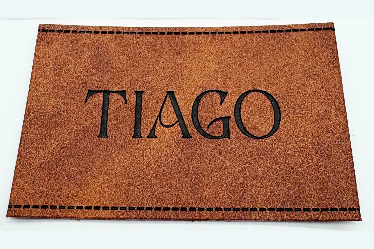 A brown rectangular leather label with black lettering and stitched edges.