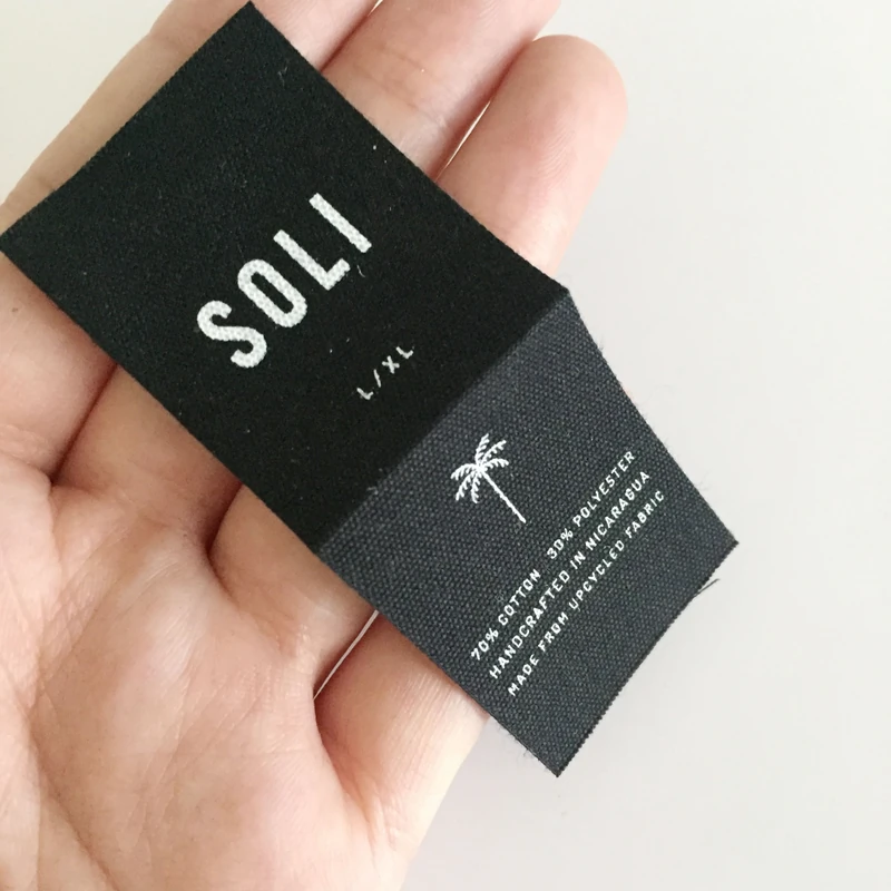 A black printed fabric label held to show its texture.