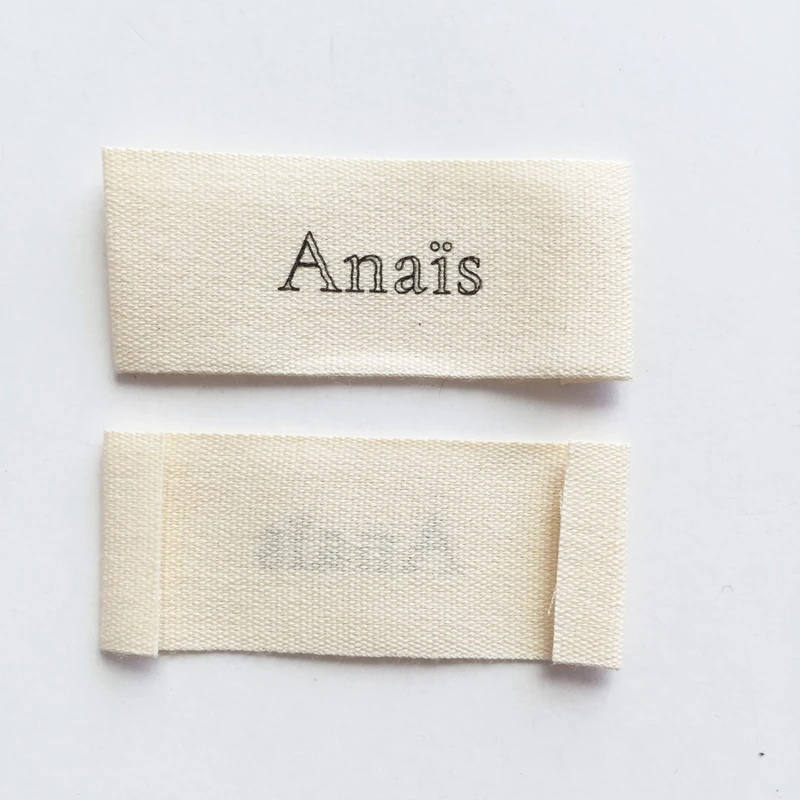 A printed fabric label showing its front and folded ends.
