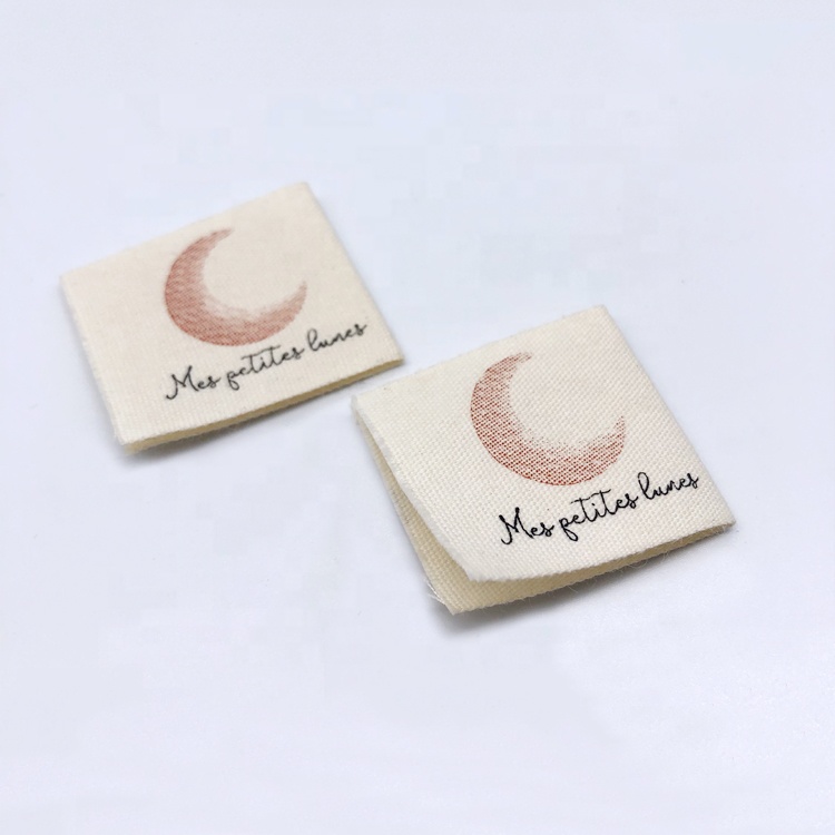 Two cream printed fabric labels with brown crescent moons and black lettering.