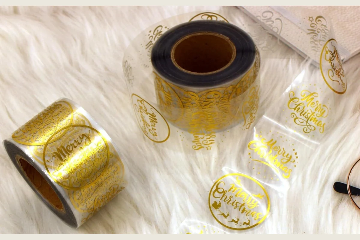 Transparent sticker rolls with gold Christmas printing and an unfolded label strip.