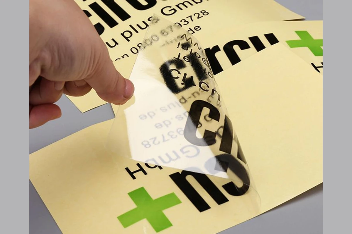 A hand peeling a printed transparent sticker from a yellow release liner.