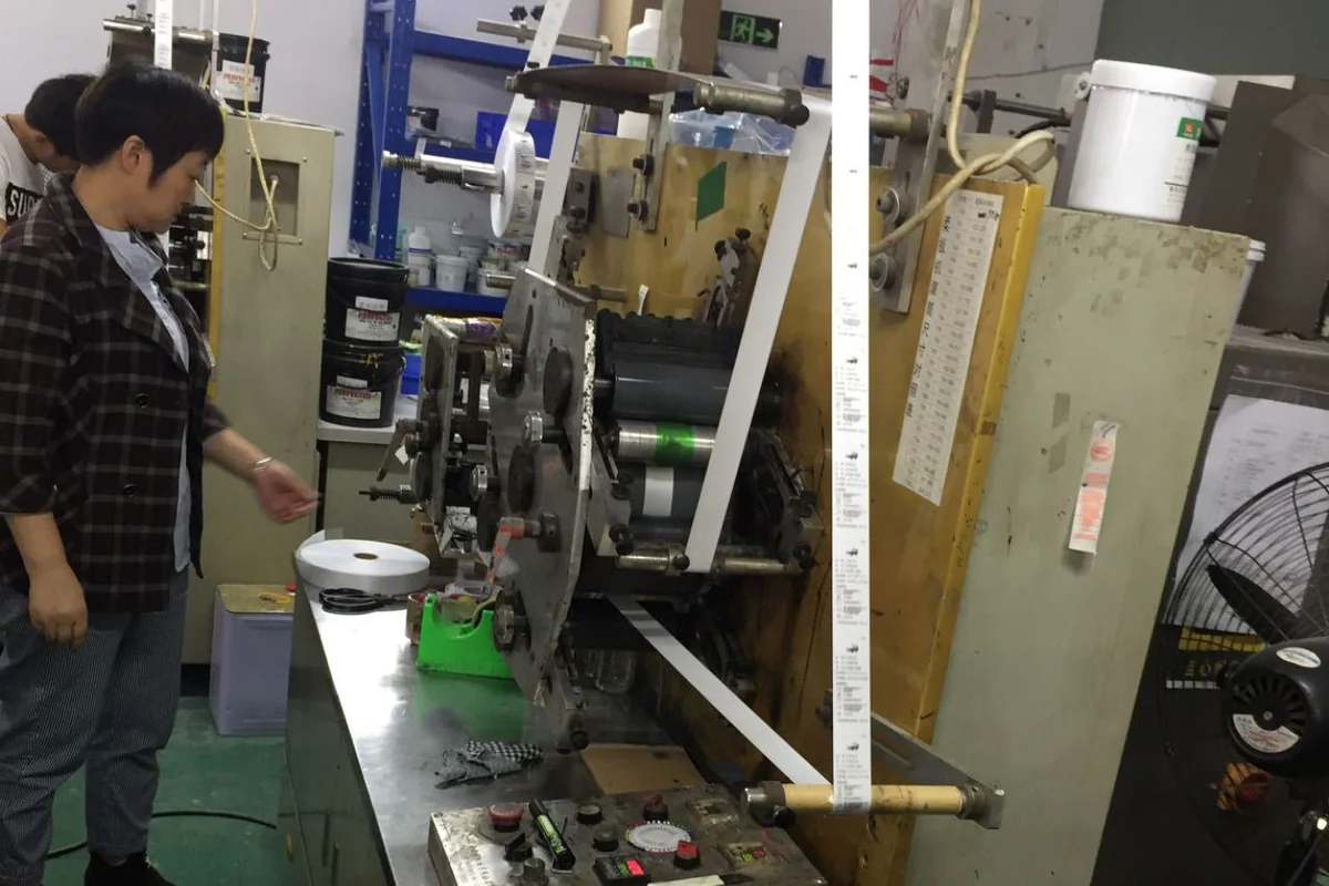 An operator beside a machine carrying a narrow roll of printed labels.