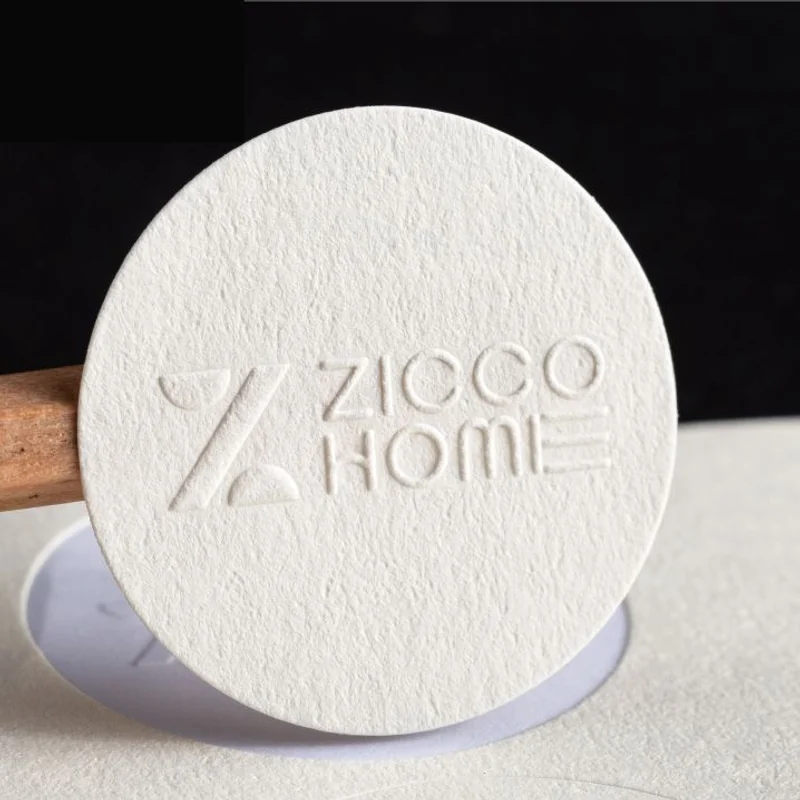 A round textured paper sticker with raised lettering.