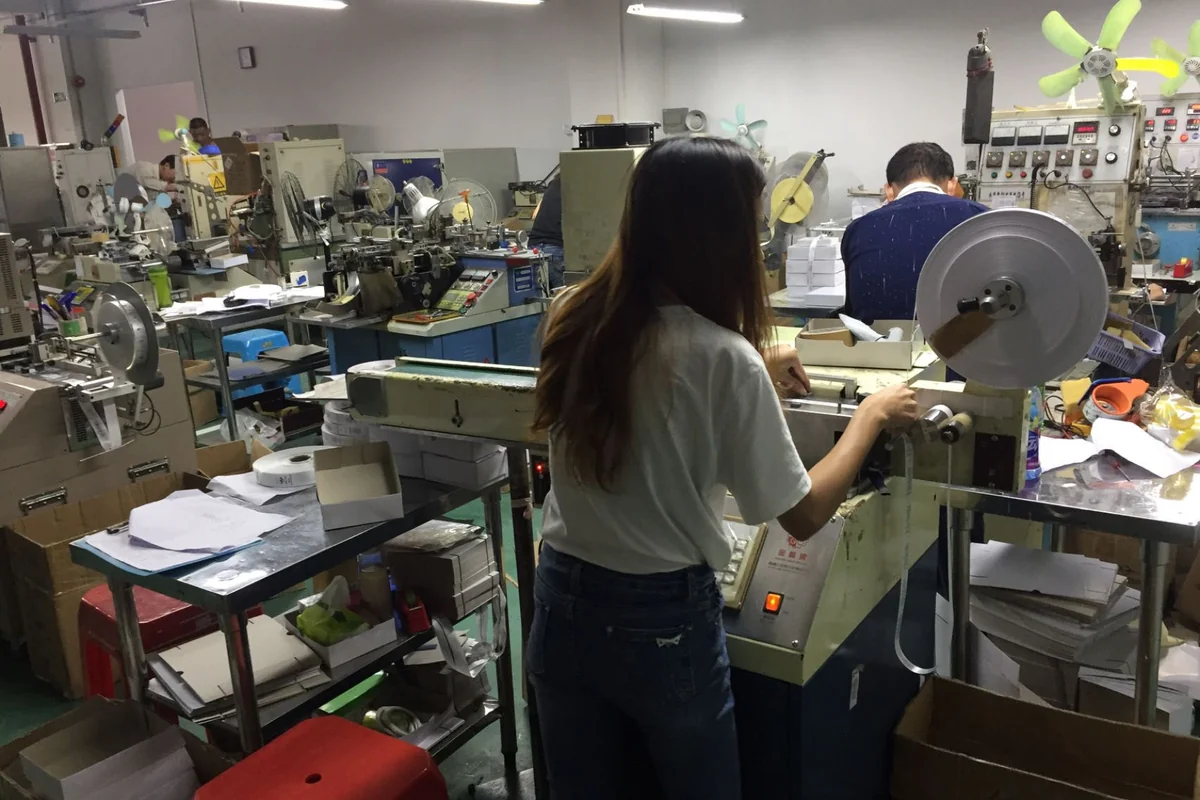 Workers handling label rolls at equipment in a workshop.