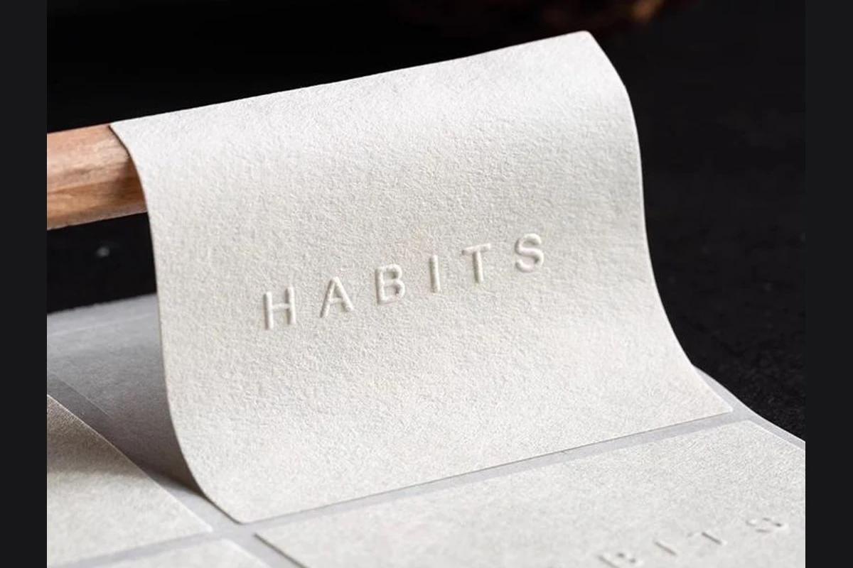 A curled white paper sticker with spaced raised brand lettering.