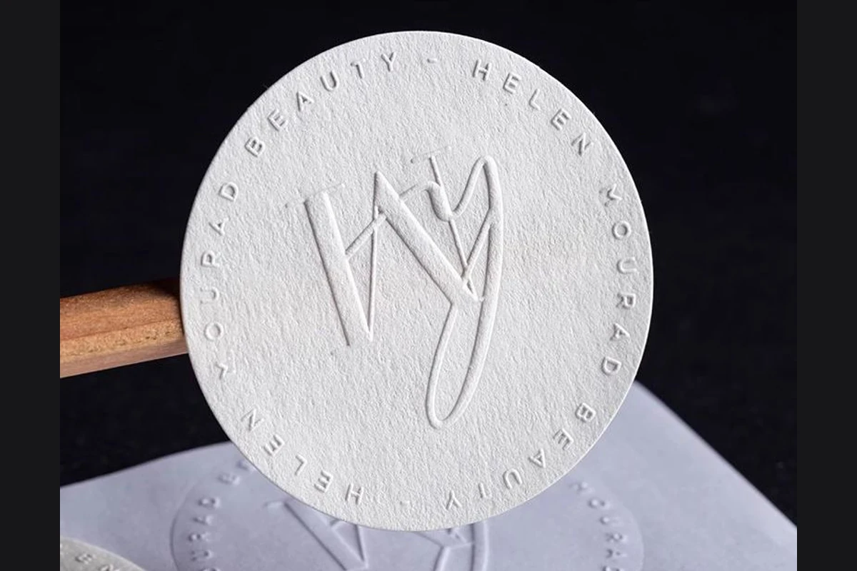 A round paper sticker with a raised monogram and border lettering.