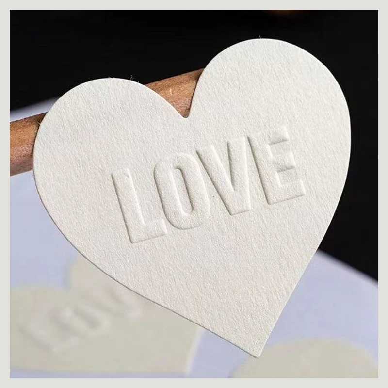 A white heart-shaped paper sticker with raised lettering.