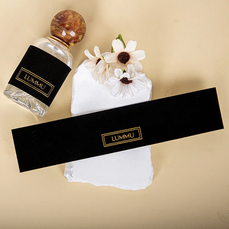 Black adhesive brand-label samples with gold lettering beside a perfume bottle.
