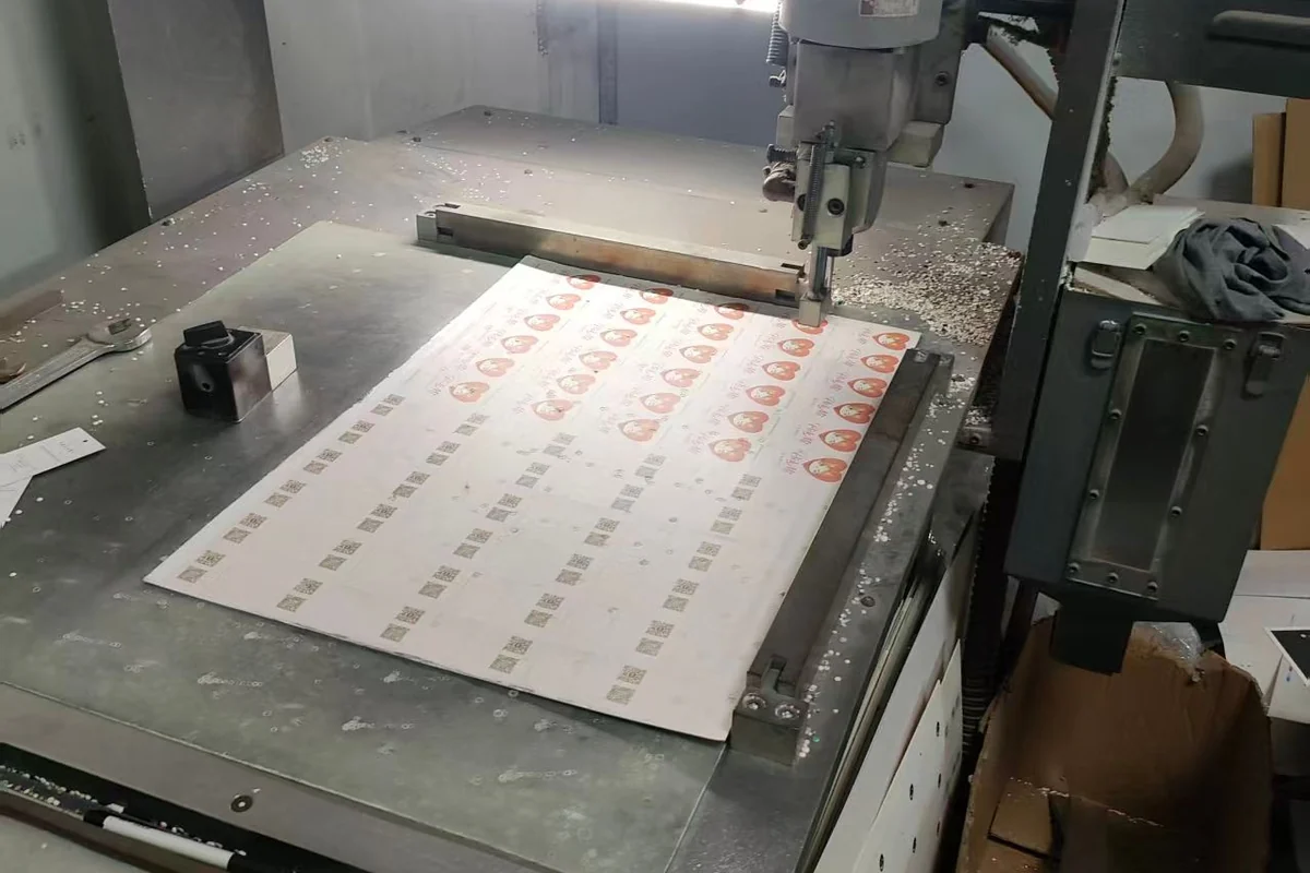 A production tool positioned above repeated designs on a printed sheet.