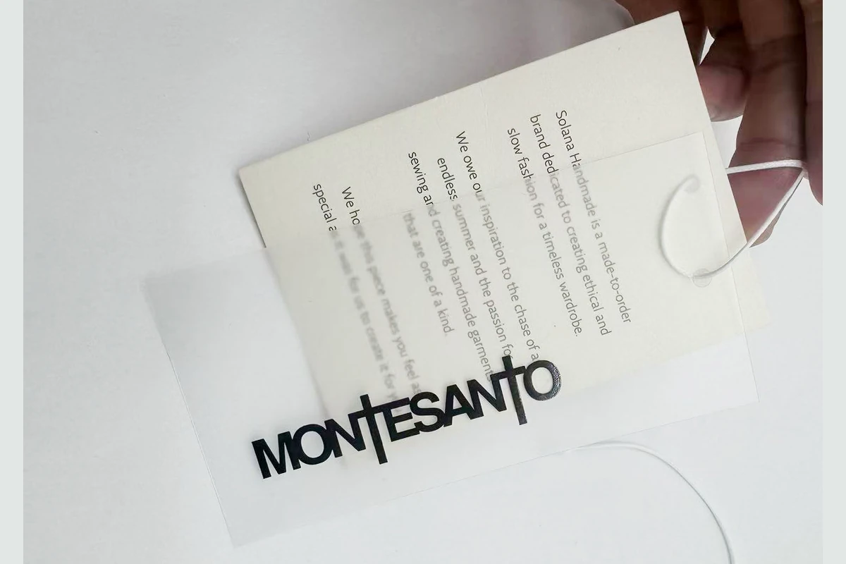 A hand holding layered paper and transparent printed hang-tag samples.
