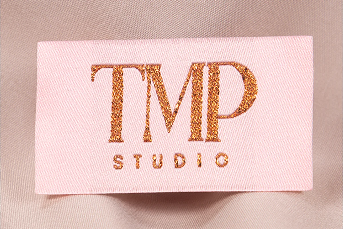 A pink woven label with gold lettering on fabric.
