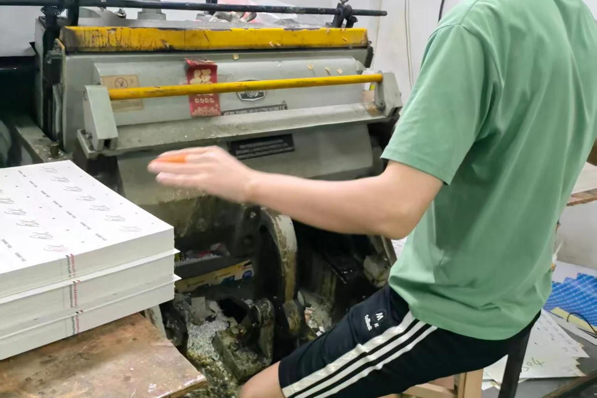 An operator beside a stack of printed sheets at a production station.